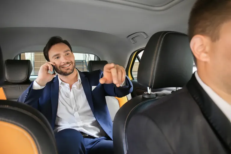 Otomobilin arka koltuğunda telefonla konuşan yolcu ve öndeki sürücü